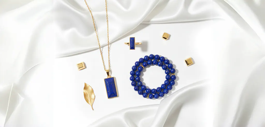 Elegant flat lay of lapis lazuli jewelry set on white silk with gold accents.